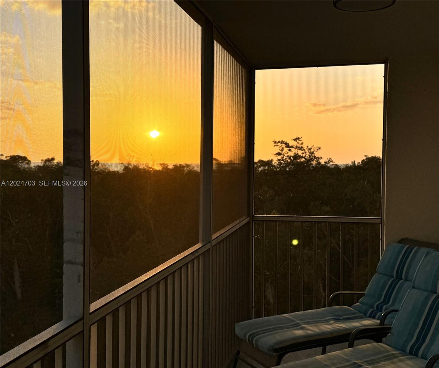A screened-in balcony features two lounge chairs overlooking a sunset over trees and water — 5 Bluebill # 403, Naples FL 34108, NAPLES, FL