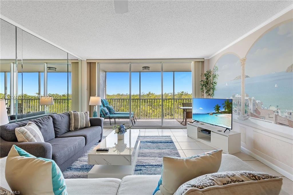 A living room features a gray sofa, a television, and a large mural wall painting — 5 Bluebill # 403, Naples FL 34108, NAPLES, FL