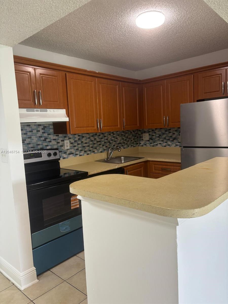 A kitchen features wood cabinets, a tiled backsplash, stainless steel appliances, and a breakfast bar — 7110 NW 179th St # 211, Hialeah FL 33015, HIALEAH, FL