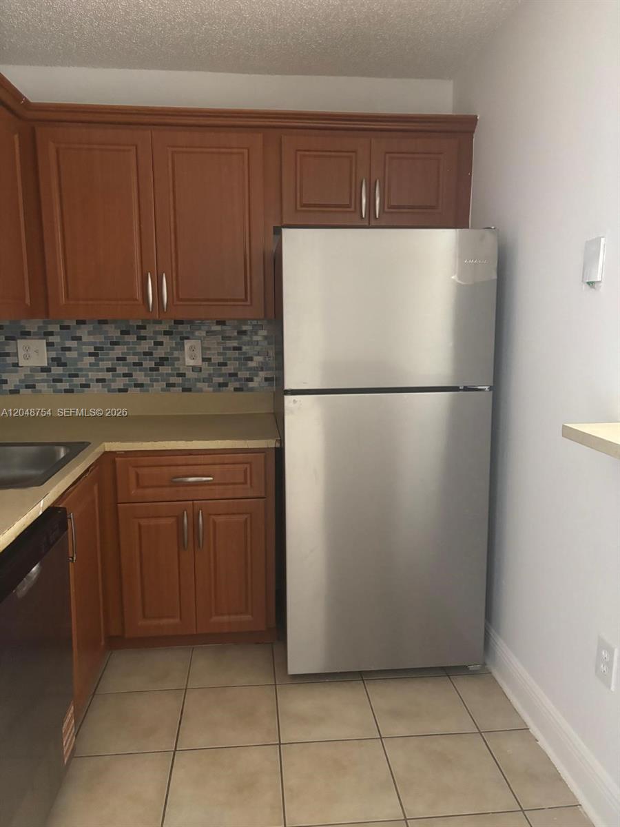 A kitchen features wood cabinets, a stainless steel refrigerator, and a blue mosaic tile backsplash — 7110 NW 179th St # 211, Hialeah FL 33015, HIALEAH, FL