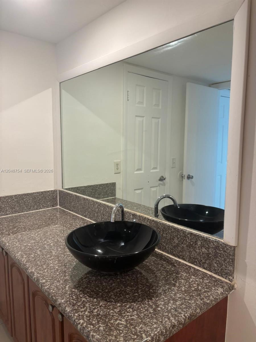 A bathroom vanity features a speckled granite countertop, a black vessel sink, and a mirror — 7110 NW 179th St # 211, Hialeah FL 33015, HIALEAH, FL
