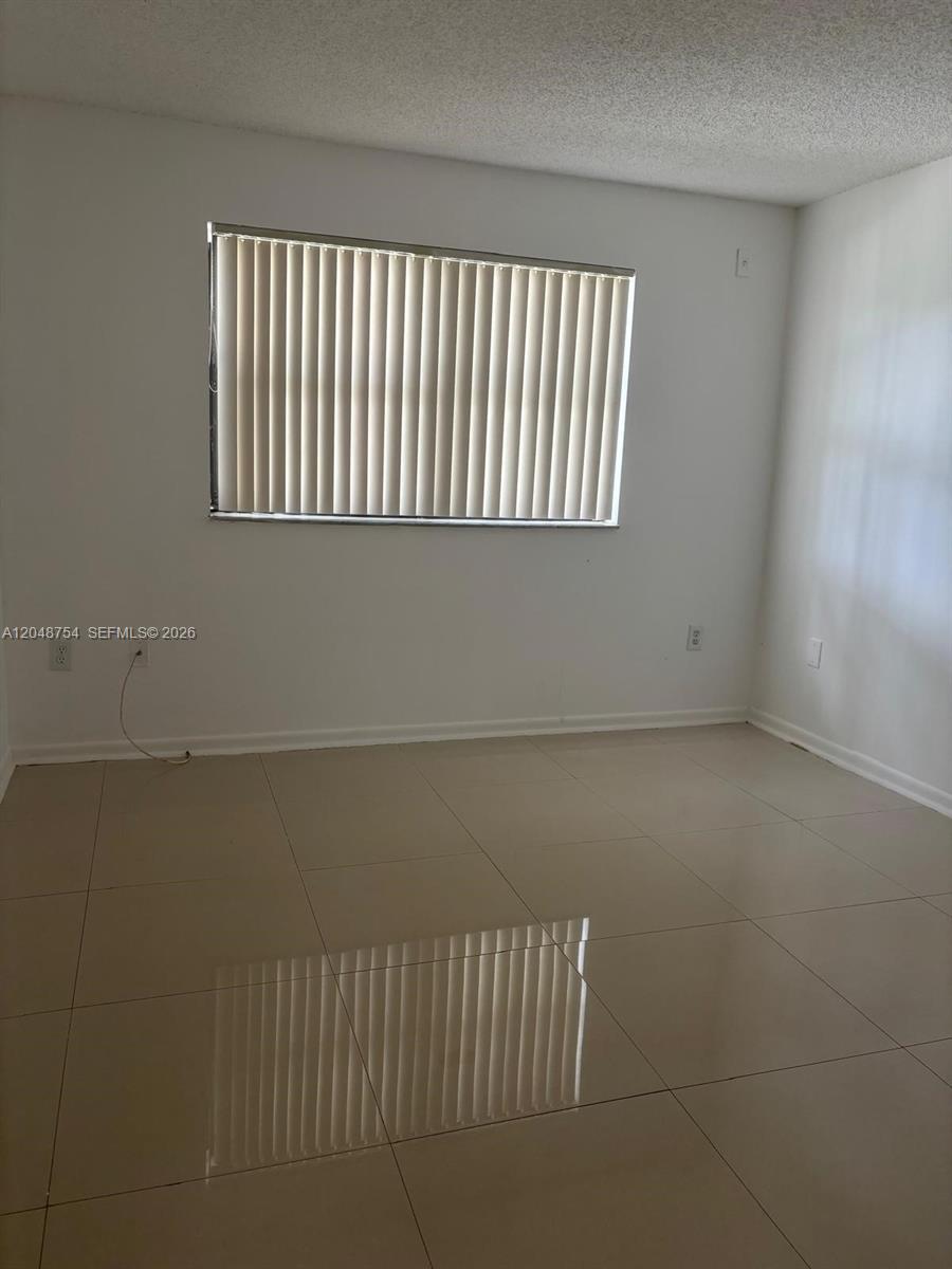An empty room features light-colored tile flooring, white walls, and a window with vertical blinds — 7110 NW 179th St # 211, Hialeah FL 33015, HIALEAH, FL