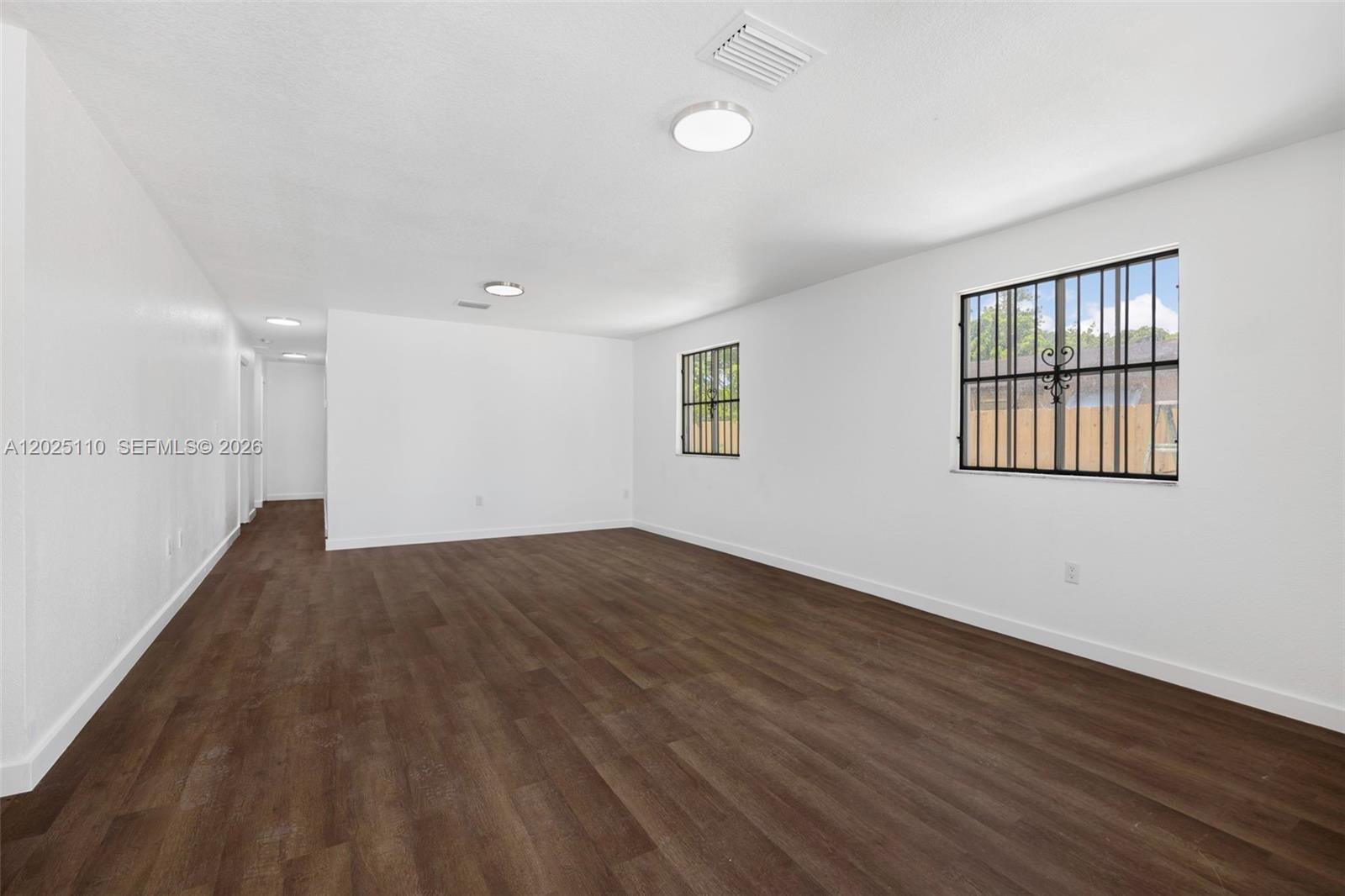 A bright, empty room features white walls, dark wood-look flooring, and two windows with grilles — 10204 SW 173rd St, Miami FL 33157, MIAMI, FL