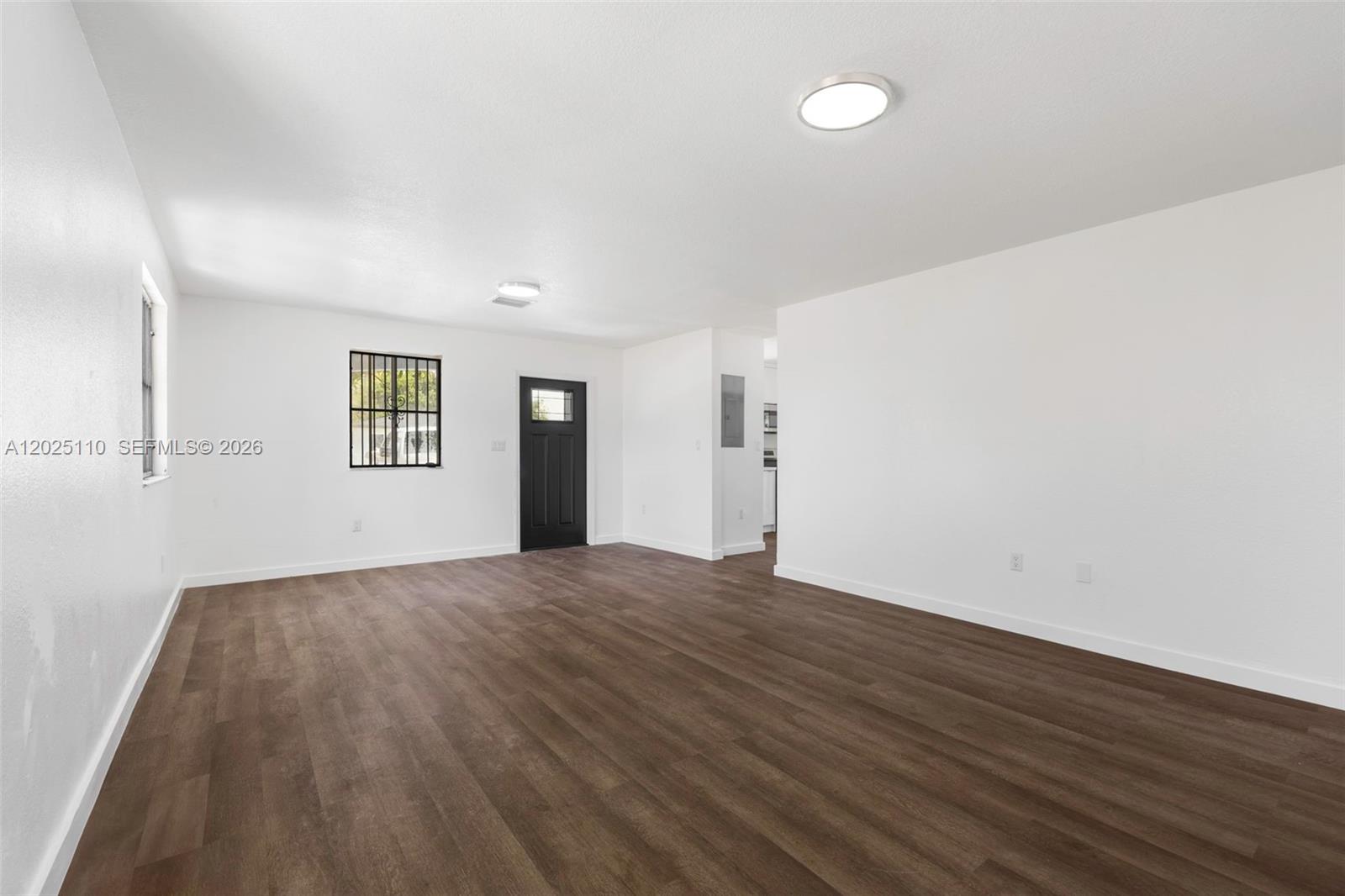 A bright, empty living room features white walls, dark wood-look flooring, and a black door — 10204 SW 173rd St, Miami FL 33157, MIAMI, FL
