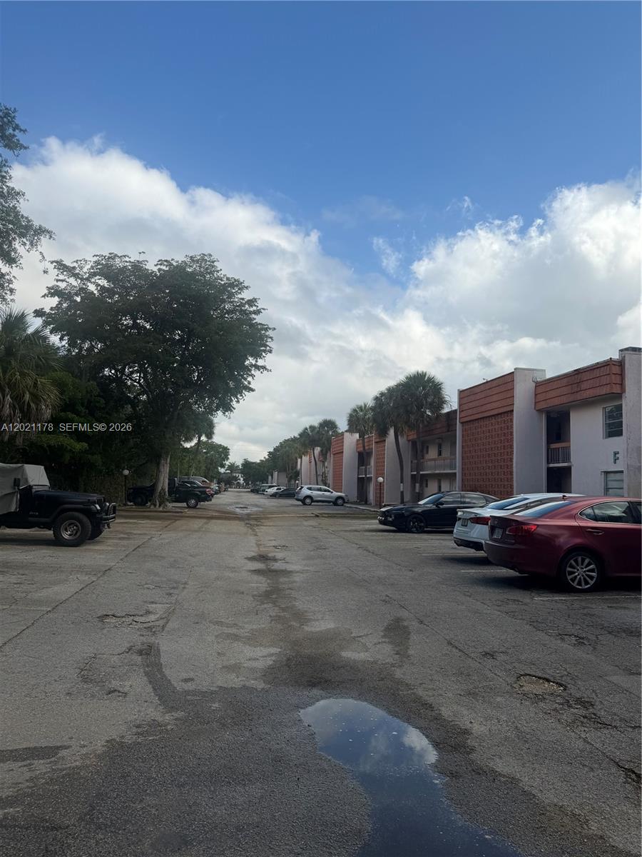 An outdoor parking lot sits between two-story apartment buildings with palm trees and parked cars — 7610 Stirling Rd # 205G, Davie FL 33024, DAVIE, FL