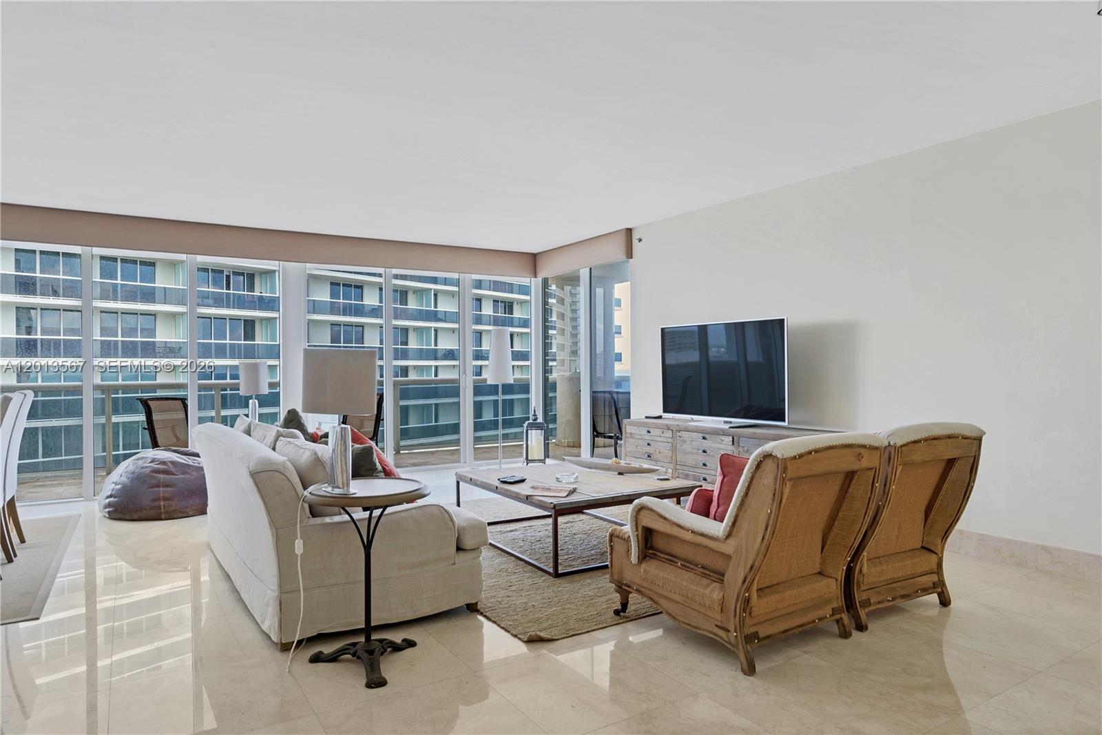 A living room features a sofa, two wooden armchairs, a coffee table, and floor-to-ceiling windows — 1850 S Ocean Dr # 1410, Hallandale Beach FL 33009, HALLANDALE BEACH, FL