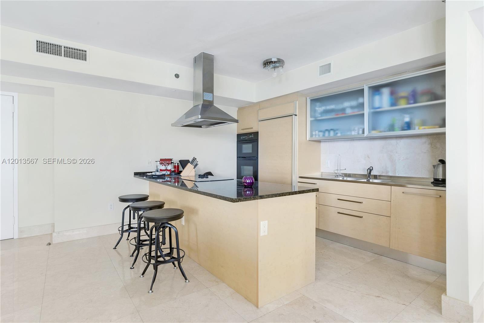 A modern kitchen features light wood cabinetry, a black granite island, and three metal stools — 1850 S Ocean Dr # 1410, Hallandale Beach FL 33009, HALLANDALE BEACH, FL
