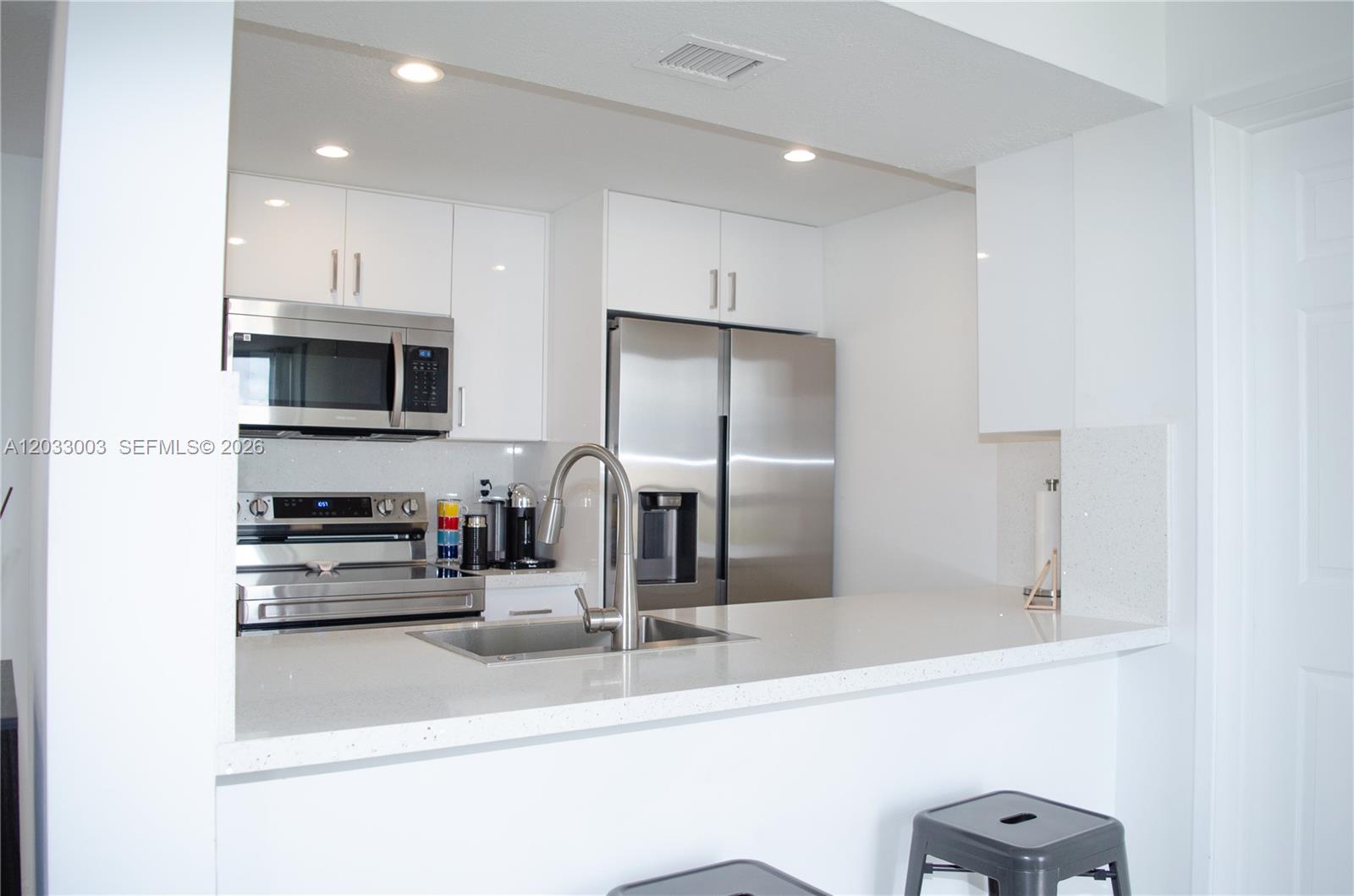 A kitchen features white cabinets, stainless steel appliances, and a white quartz countertop breakfast bar — 6995 NW 186th St # E509, Hialeah FL 33015, HIALEAH, FL
