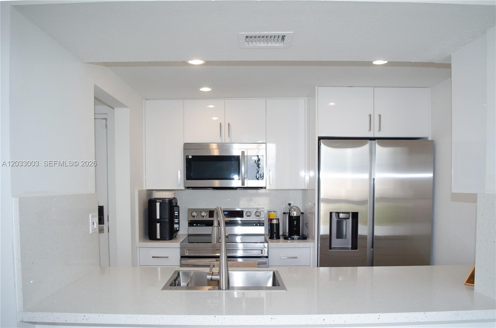 A modern kitchen features white cabinetry, stainless steel appliances, and a quartz countertop island — 6995 NW 186th St # E509, Hialeah FL 33015, HIALEAH, FL