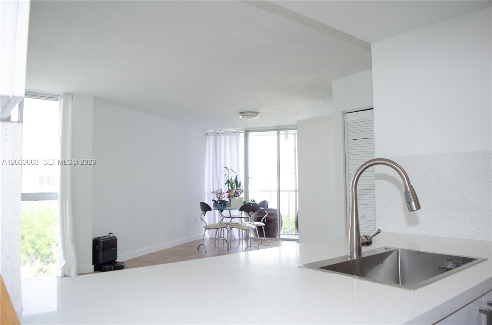 A kitchen sink and countertop overlook a dining area with a glass table and balcony — 6995 NW 186th St # E509, Hialeah FL 33015, HIALEAH, FL
