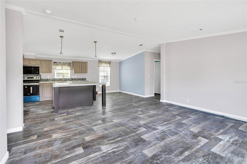 An open-concept kitchen and living area features wood-look flooring, a center island, and neutral walls — 3264 STEPHENS BOULEVARD, SPRING HILL, FL