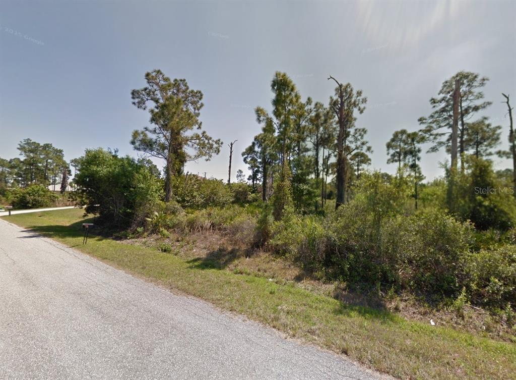 A vacant, wooded residential lot sits alongside a paved road under a clear sky — 23193 ALASKA AVENUE, PORT CHARLOTTE, FL