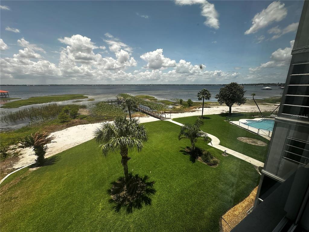 A view from a balcony overlooking a grassy lawn, palm trees, a pool, and water — 2131 LAKEVIEW DRIVE UNIT 410, SEBRING, FL
