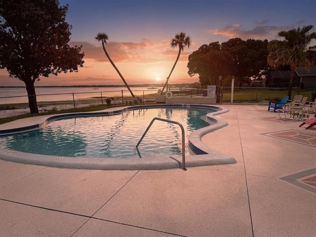 A swimming pool overlooks a lake at sunset with palm trees and patio furniture nearby — 2131 LAKEVIEW DRIVE UNIT 410, SEBRING, FL