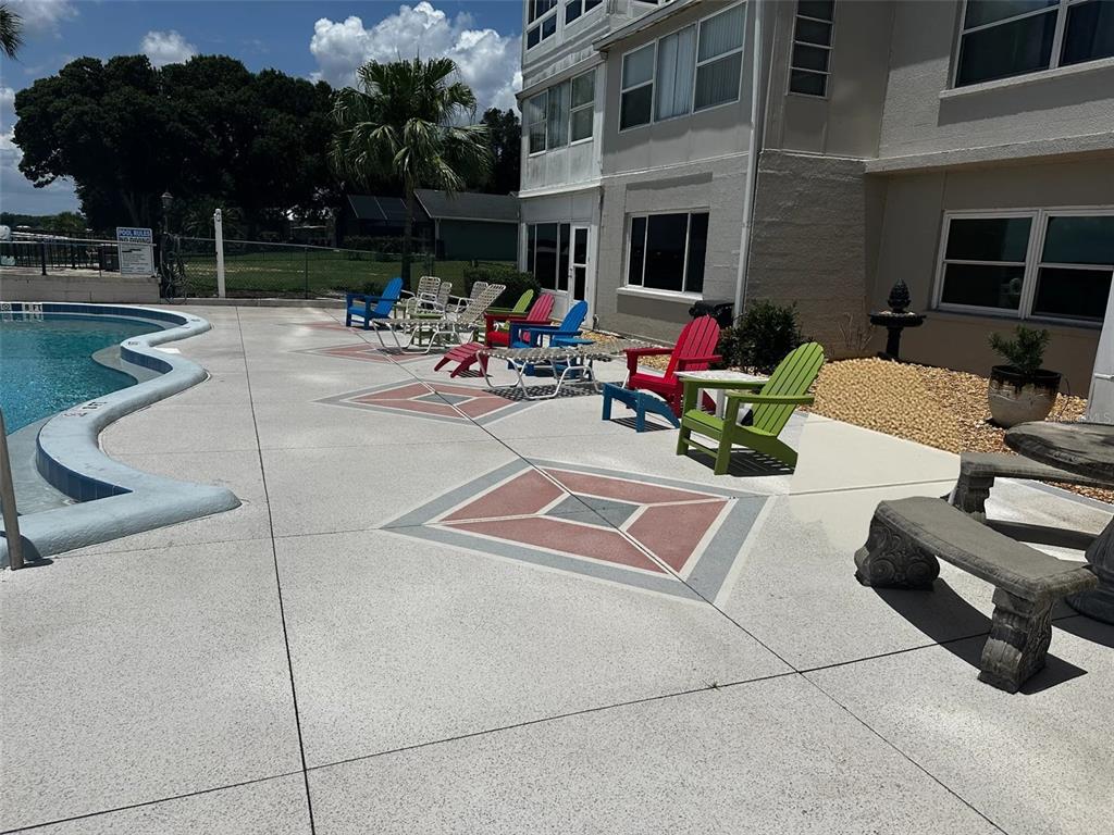 A swimming pool deck features colorful Adirondack chairs, stone benches, and a multi-story building exterior — 2131 LAKEVIEW DRIVE UNIT 410, SEBRING, FL