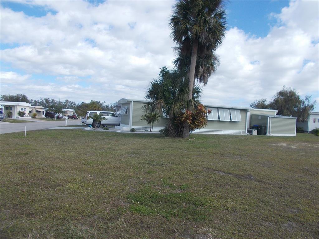 A light green mobile home with white shutters sits on a grassy lot with palm trees — 6466 KILOHEE COURT, NORTH PORT, FL