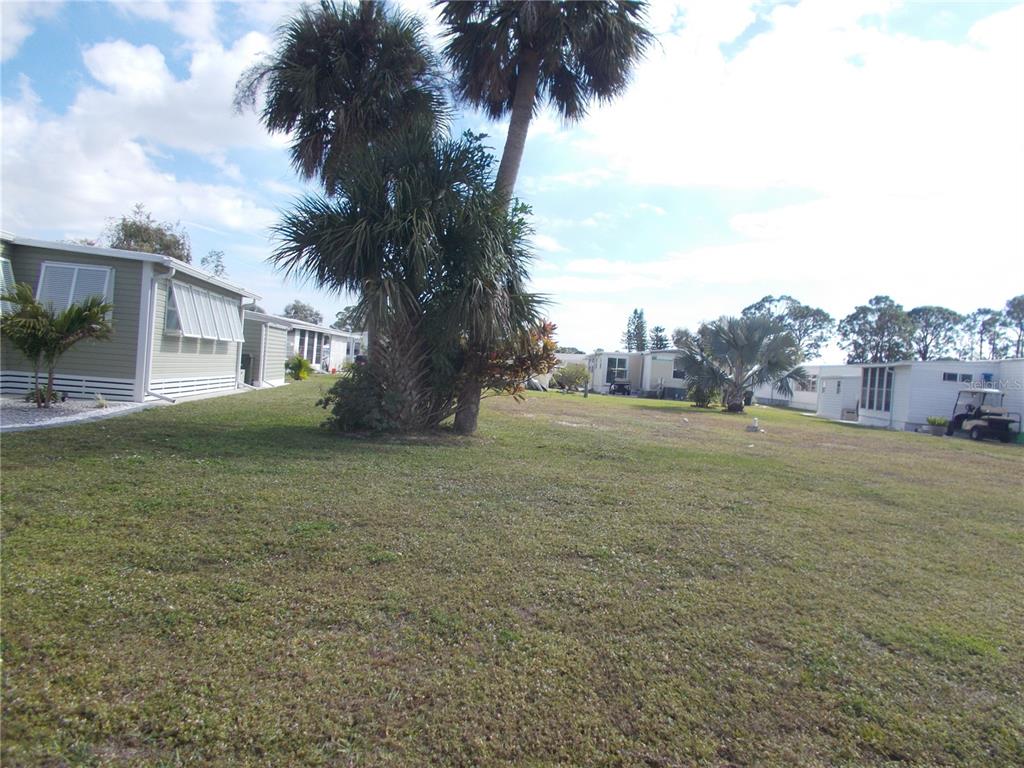 A grassy lot with palm trees is situated between several manufactured homes — 6466 KILOHEE COURT, NORTH PORT, FL