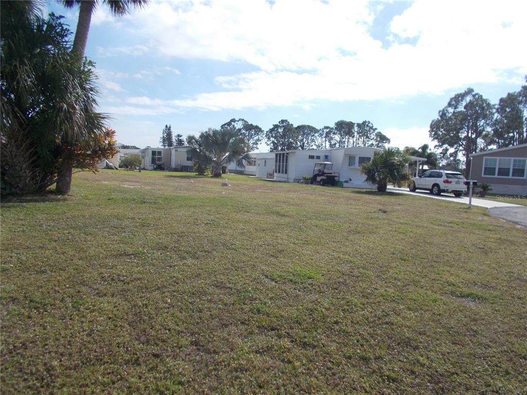 A grassy vacant lot sits adjacent to a white mobile home and a parked car — 6466 KILOHEE COURT, NORTH PORT, FL