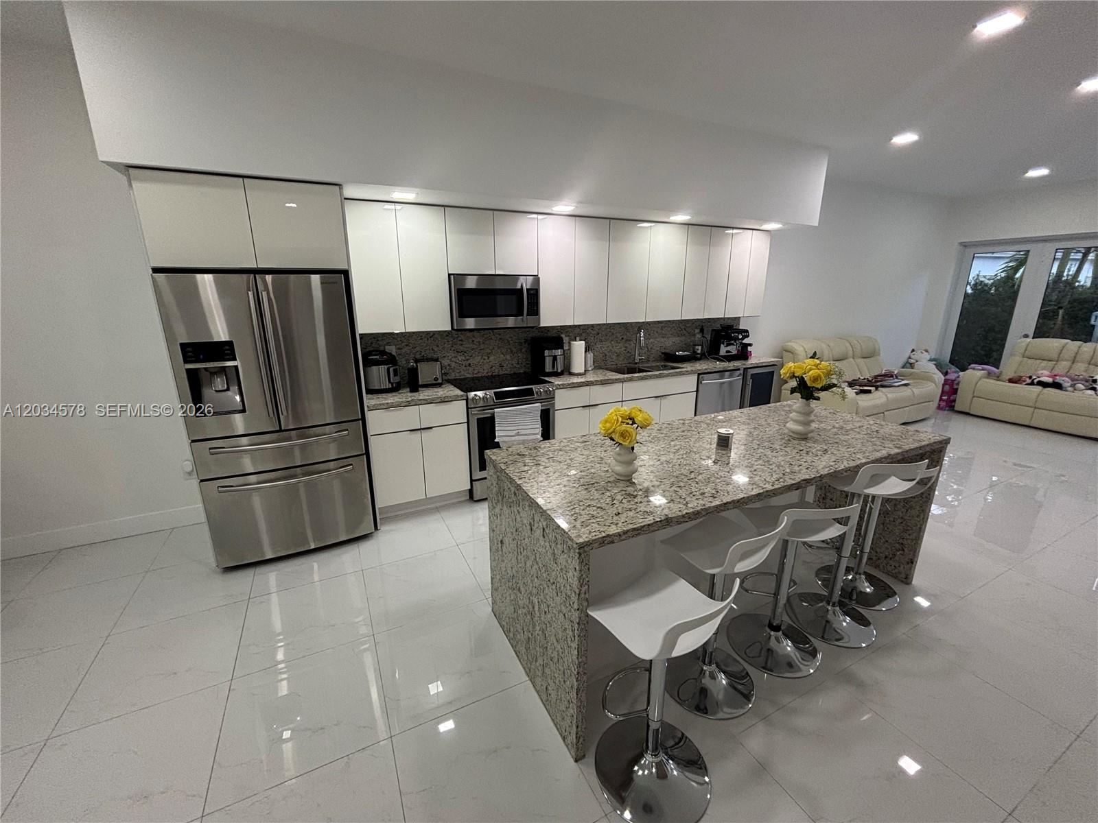A modern kitchen features white cabinetry, stainless steel appliances, and a granite-topped island with stools — 8143 SW 162nd Path, Miami FL 33193, MIAMI, FL