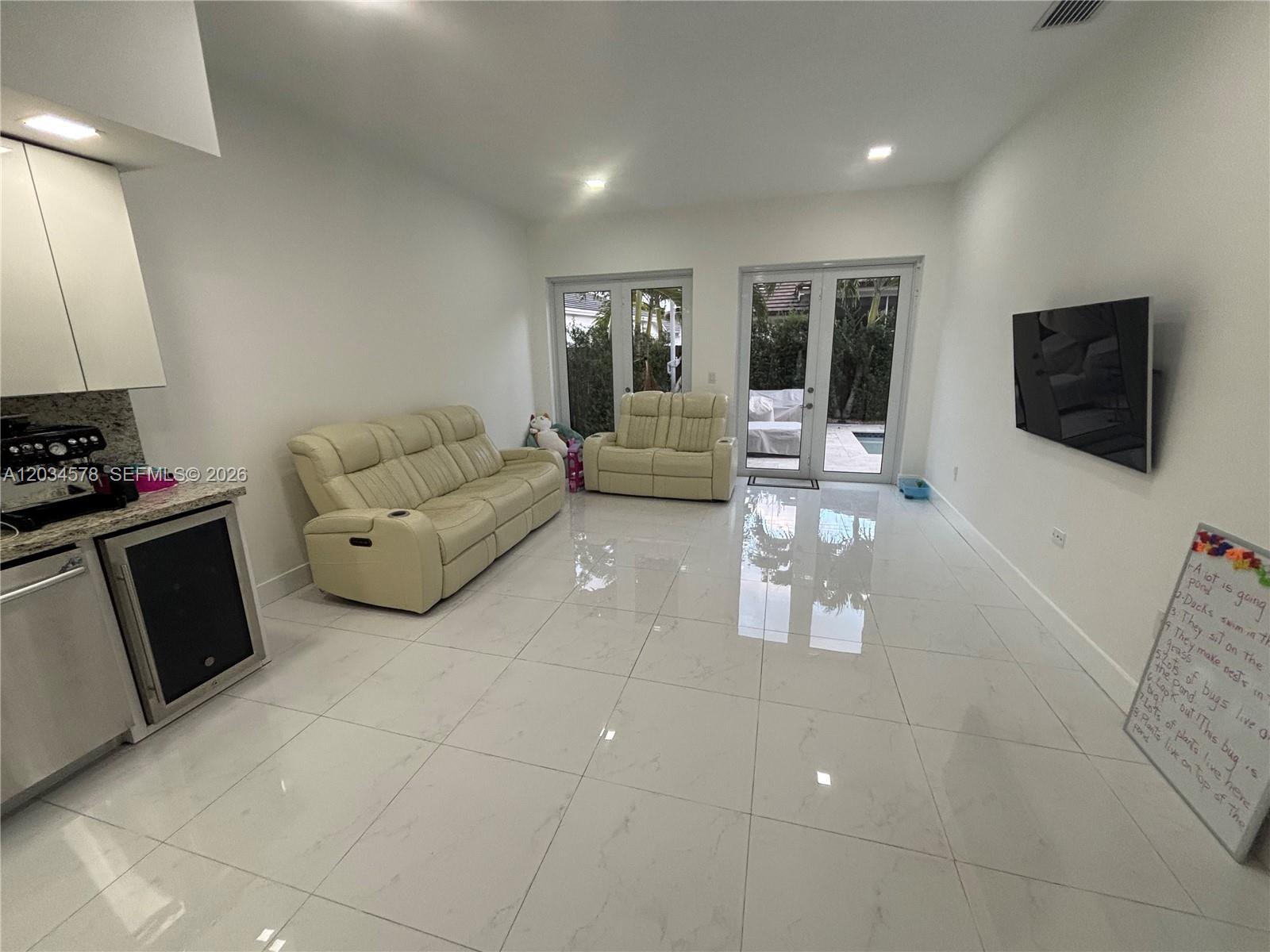 A living room with white tile floors, two cream-colored sofas, and glass doors to a patio — 8143 SW 162nd Path, Miami FL 33193, MIAMI, FL