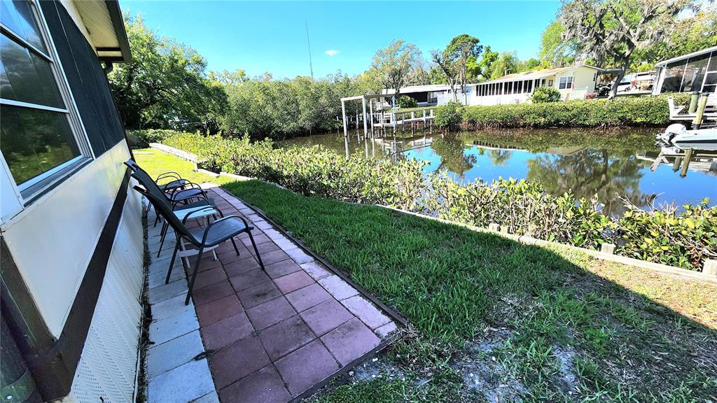 A paved patio with chairs sits beside a house overlooking a canal and trees — 3333 26TH AVENUE E UNIT 1292, BRADENTON, FL