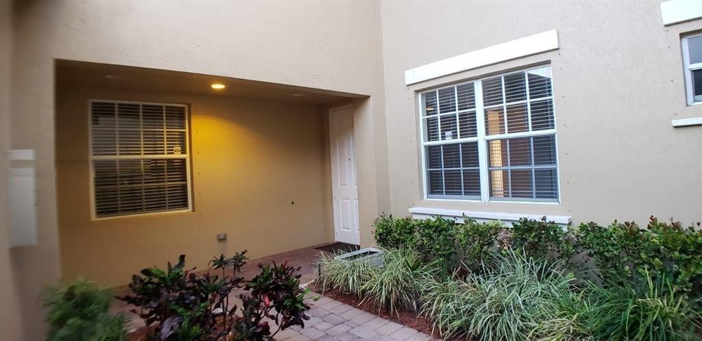 A tan exterior wall features a recessed entryway, a window with blinds, and landscaping — 8207 NW 128th Lane # b, Parkland FL 33076, PARKLAND, FL