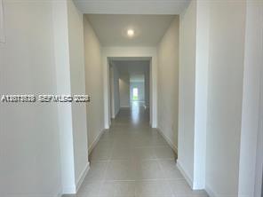 A long, narrow hallway with light-colored tile flooring leads toward a bright, open doorway — 863 SE 26th Ter # 0, Homestead FL 33035, HOMESTEAD, FL