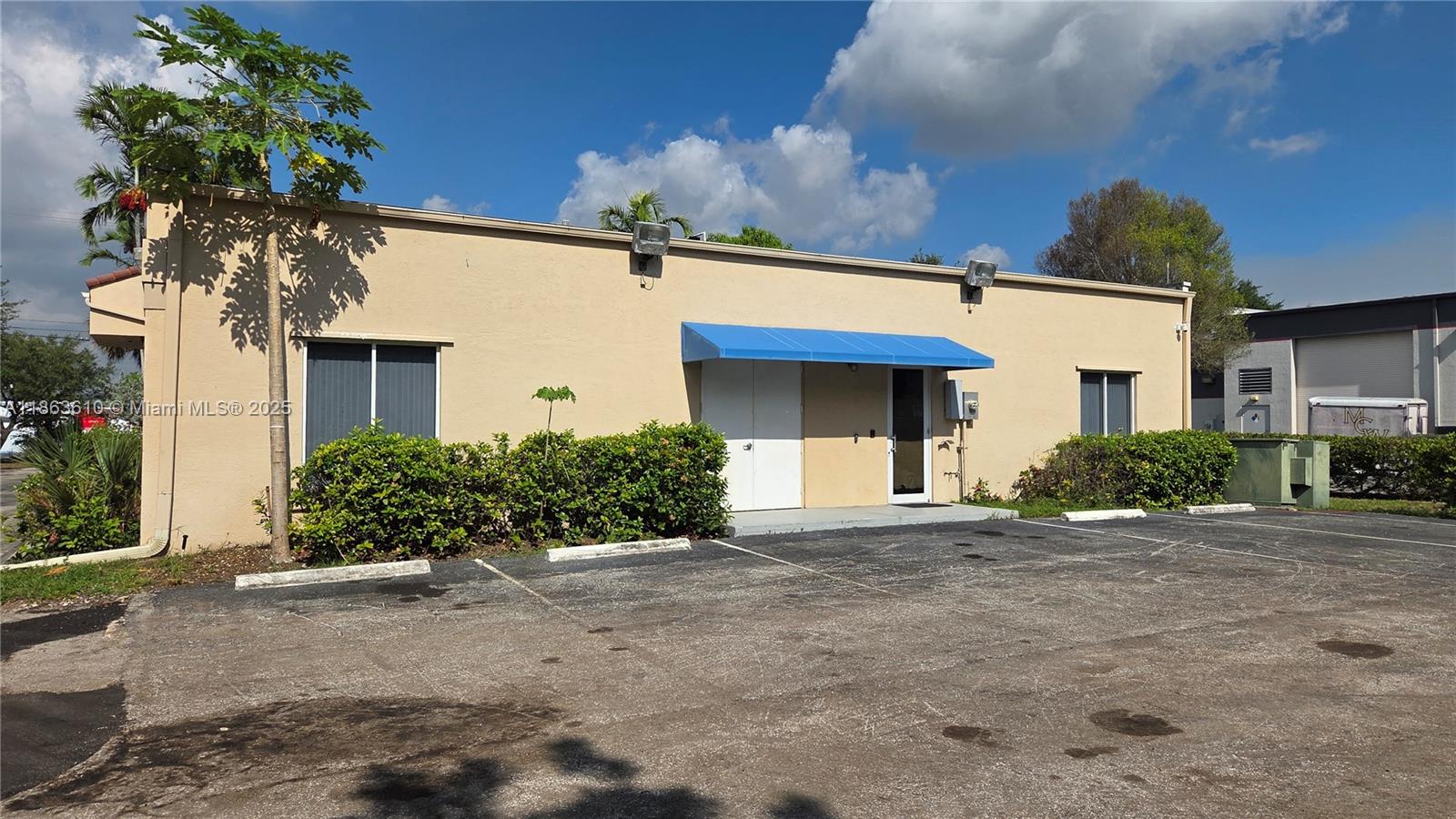 A beige commercial building features a blue awning over the entrance and a parking lot — 1150 SW 30th Ave, Pompano Beach FL 33069, POMPANO BEACH, FL