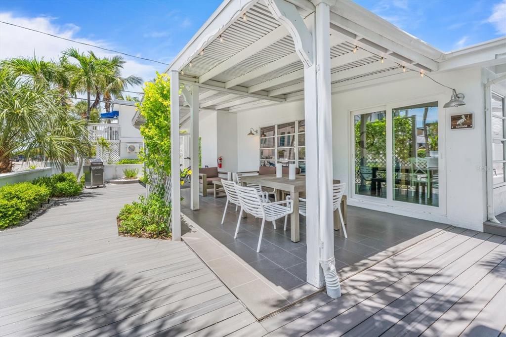 A covered outdoor patio features a dining table, white chairs, and a wooden deck — 109 14TH AVENUE, ST PETE BEACH, FL