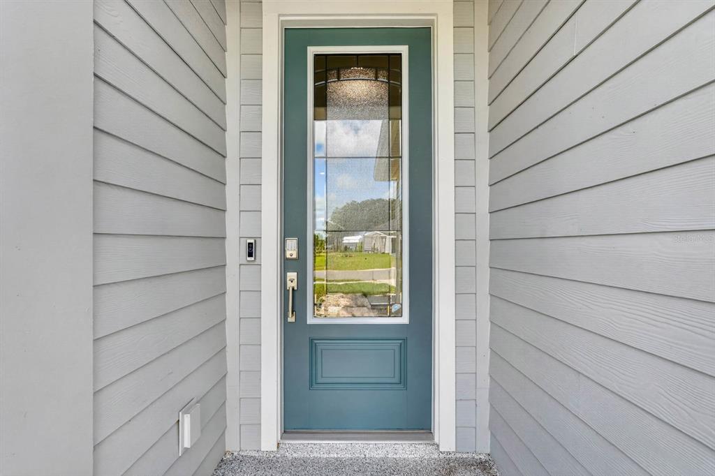 A teal front door with a glass insert is centered between light gray horizontal siding — 2173 RAGLAN CIRCLE, ORMOND BEACH, FL