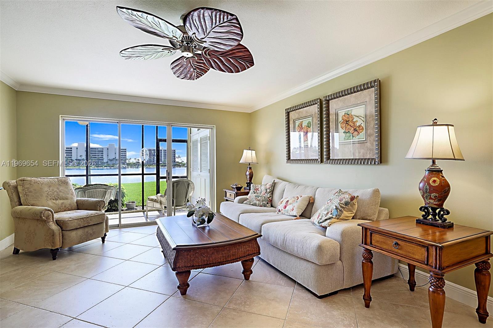 A living room features a leaf-shaped ceiling fan, beige sofa, and sliding doors overlooking water — 100 Intracoastal Pl # 102, Jupiter FL 33469, JUPITER, FL