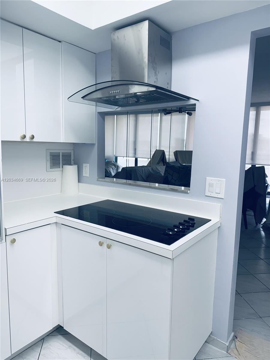 A kitchen features white cabinets, a glass-top stove, and a stainless steel range hood — 3505 S Ocean Dr # 704, Hollywood FL 33019, HOLLYWOOD, FL