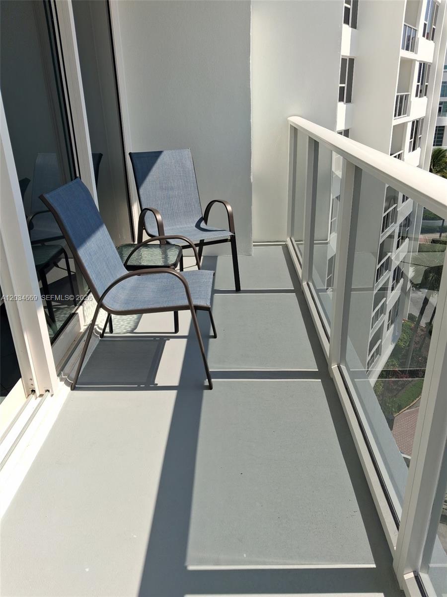 A balcony features two chairs, a small table, and a glass railing overlooking a building — 3505 S Ocean Dr # 704, Hollywood FL 33019, HOLLYWOOD, FL