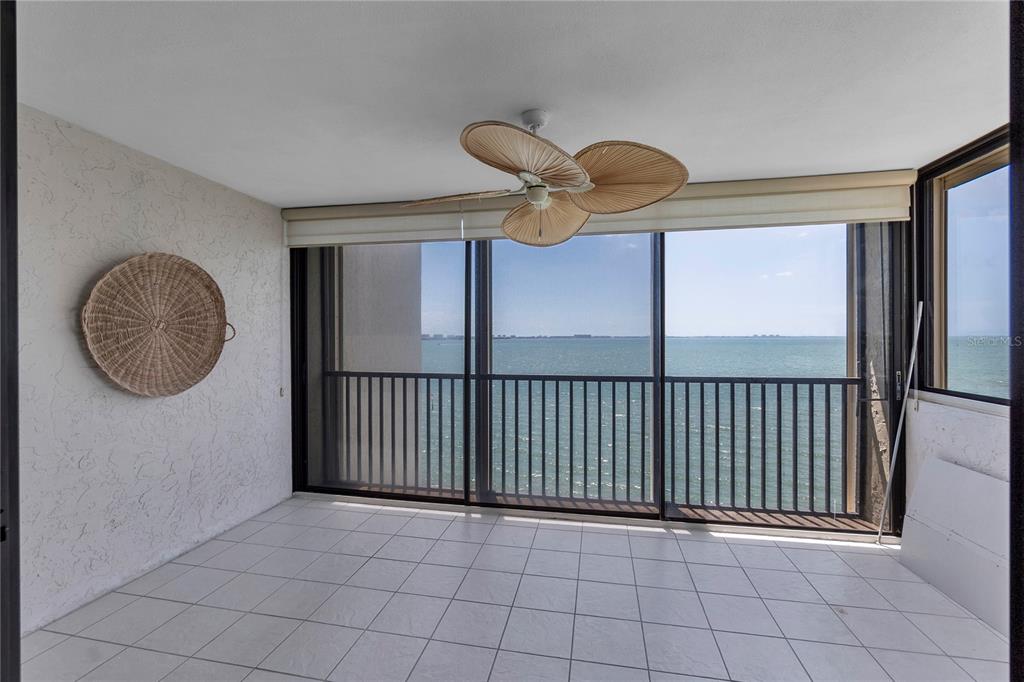 A sunroom with white tile flooring, a palm-leaf ceiling fan, and sliding glass doors overlooking water — 101 SUNSET DRIVE UNIT PH1, SARASOTA, FL
