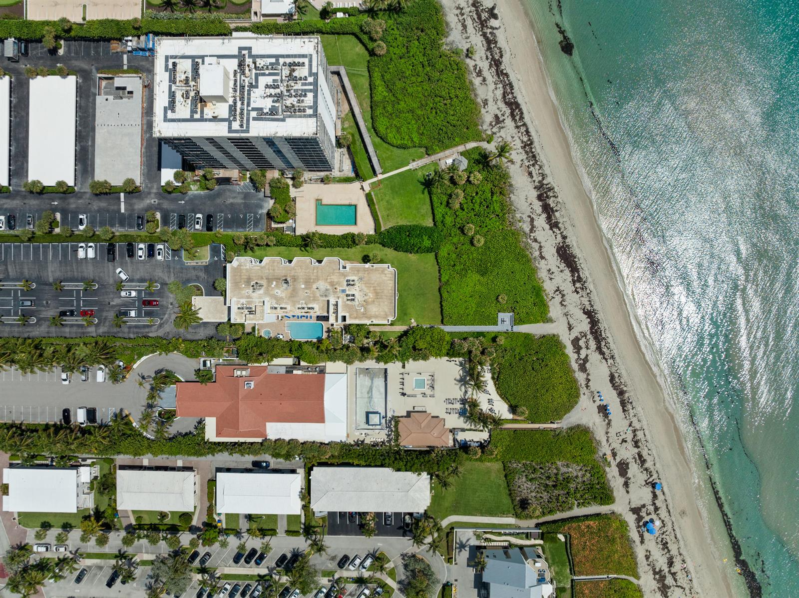An aerial view shows several beachfront buildings, parking lots, swimming pools, and a sandy coastline — 420 Celestial Way # 205, Juno Beach FL 33408, JUNO BEACH, FL