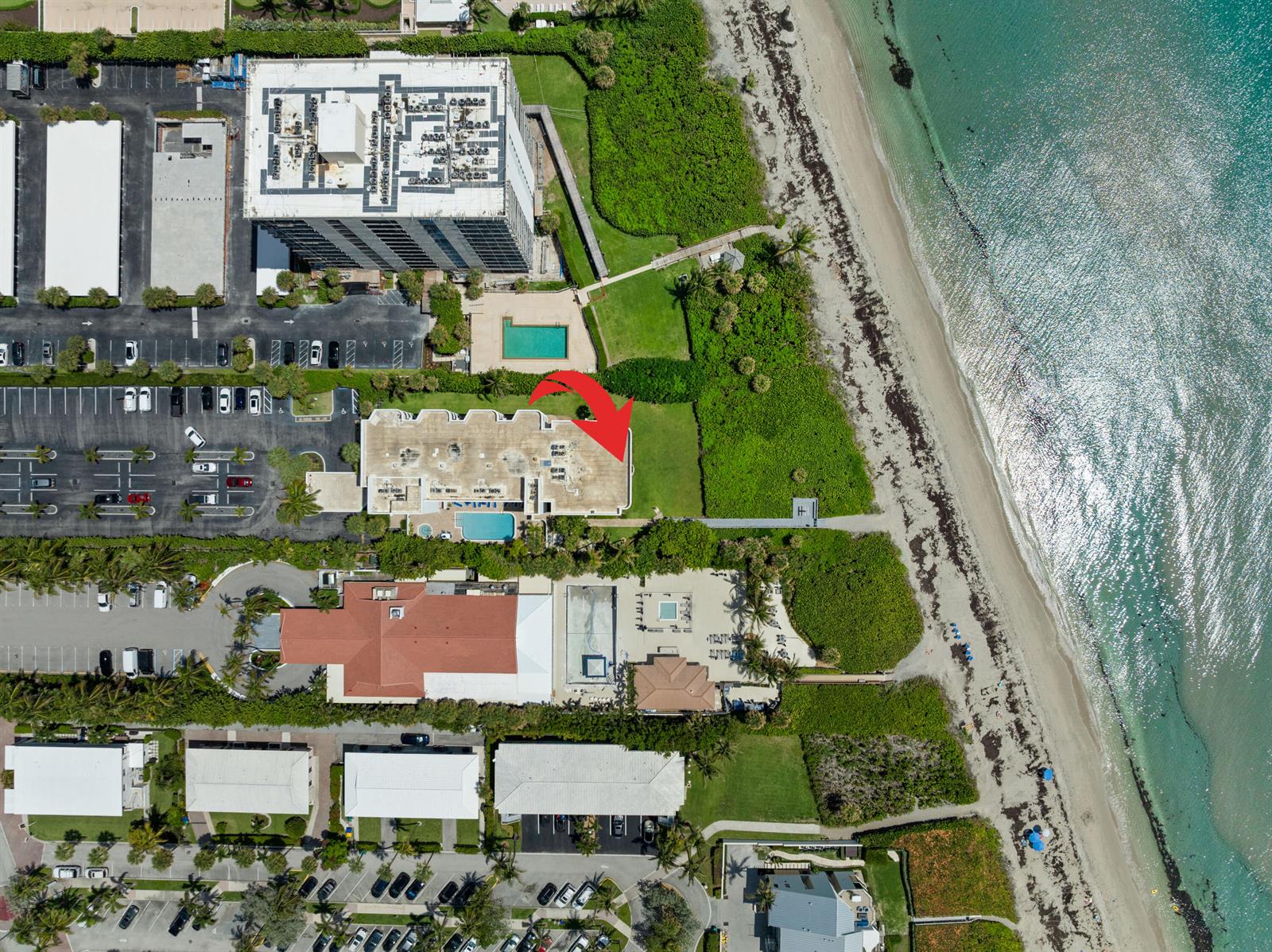 This aerial view shows a multi-story building complex with pools and parking near the beach — 420 Celestial Way # 205, Juno Beach FL 33408, JUNO BEACH, FL