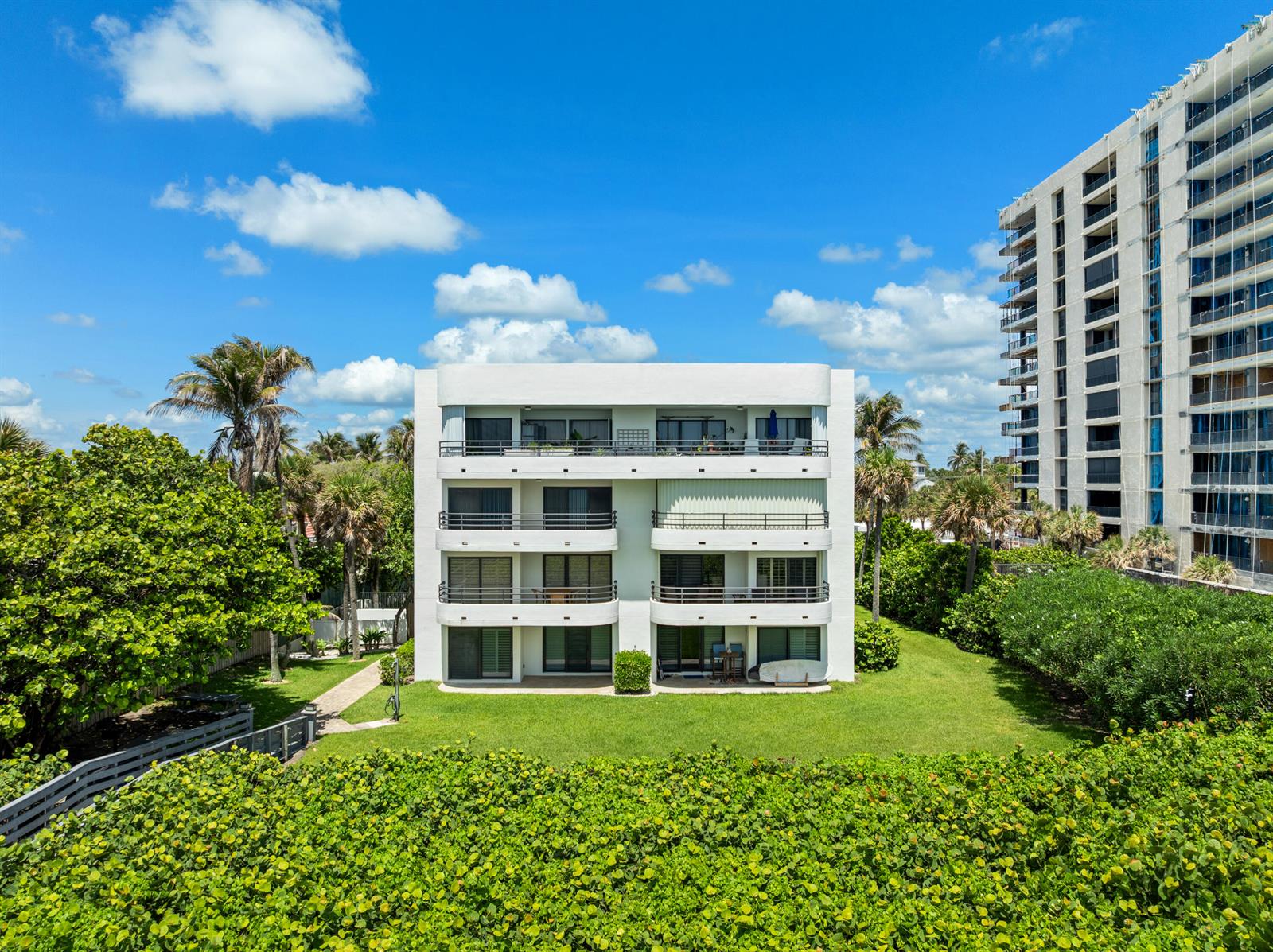 An exterior view of a four-story white apartment building surrounded by green lawns and trees — 420 Celestial Way # 205, Juno Beach FL 33408, JUNO BEACH, FL