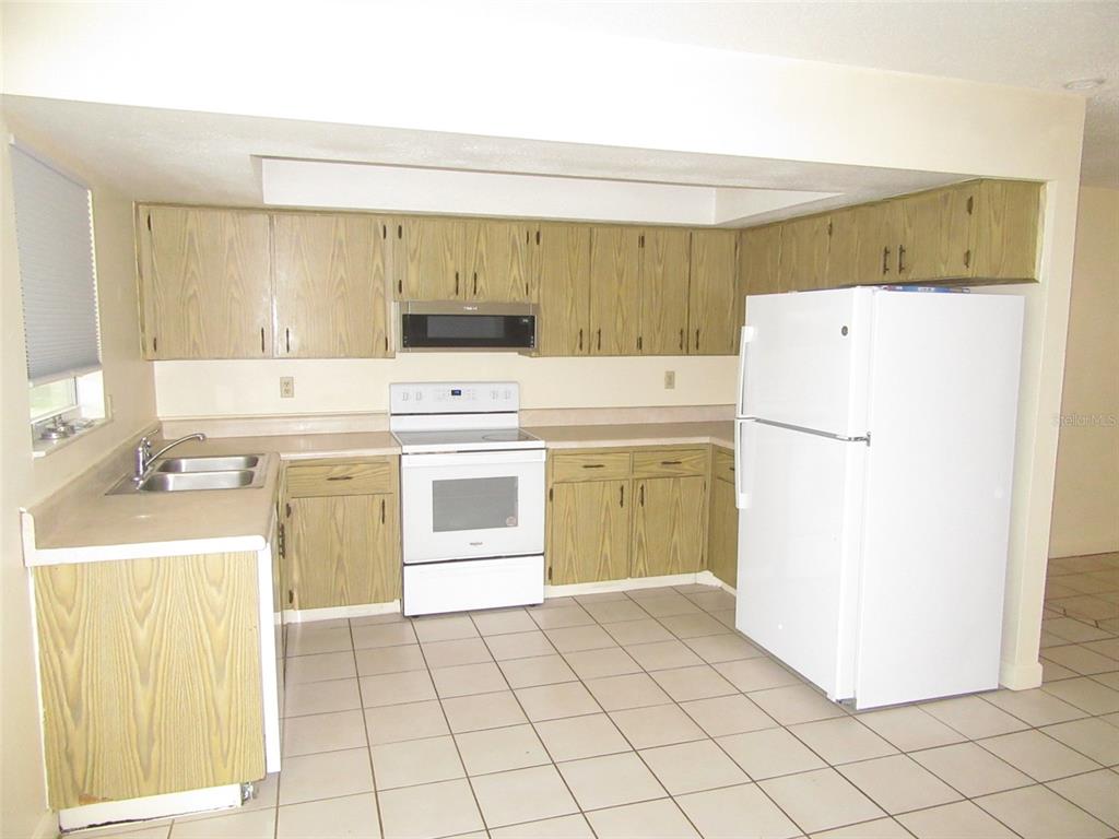 A kitchen with light wood cabinets, white appliances, beige countertops, and light-colored floor tiles — 23023 FOOTE AVENUE, PORT CHARLOTTE, FL