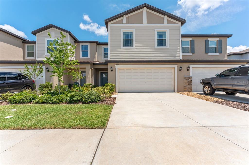 A two-story townhouse exterior features a beige facade, a two-car garage, and a concrete driveway — 32063 POP ASH PLACE, SAN ANTONIO, FL