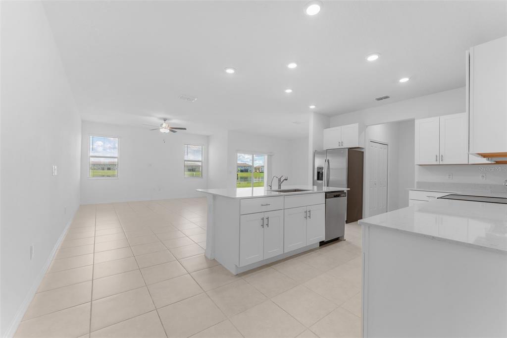 A bright open-concept kitchen and living area featuring white cabinetry, quartz countertops, and tile flooring — 32063 POP ASH PLACE, SAN ANTONIO, FL