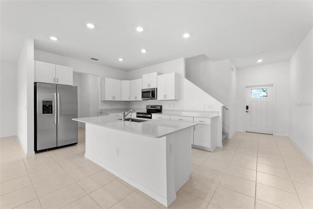A modern kitchen features white cabinetry, stainless steel appliances, a central island, and tile flooring — 32063 POP ASH PLACE, SAN ANTONIO, FL