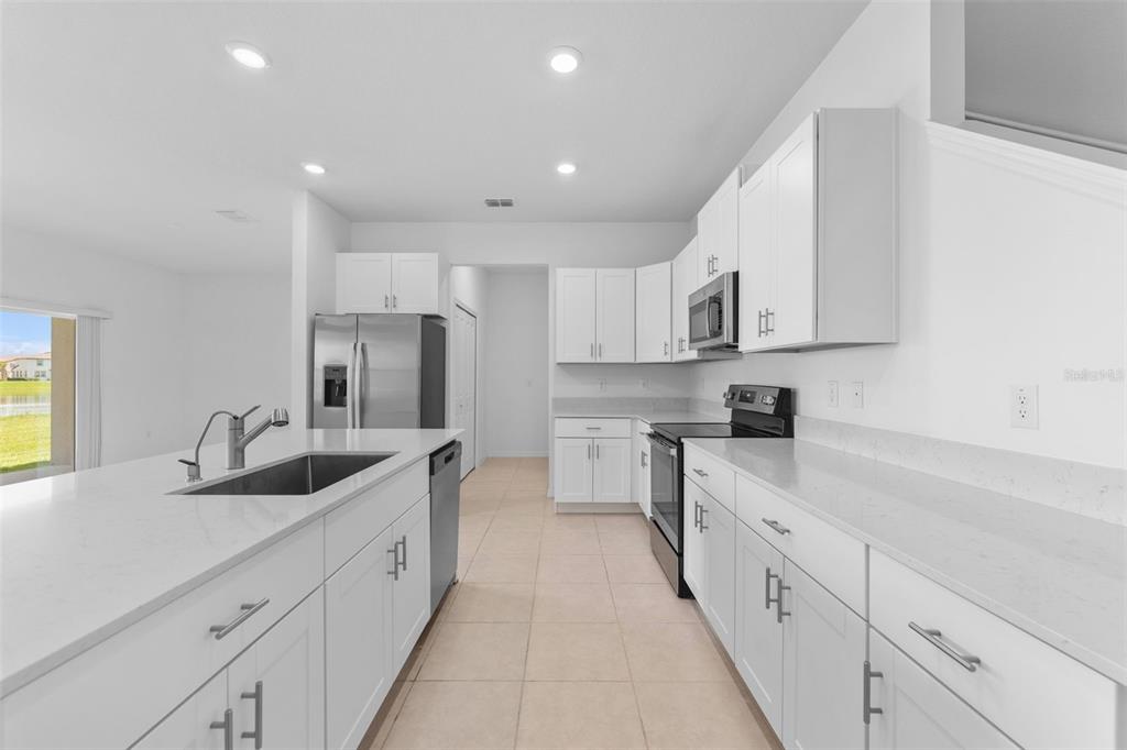A modern kitchen features white cabinets, quartz countertops, stainless steel appliances, and a central island — 32063 POP ASH PLACE, SAN ANTONIO, FL