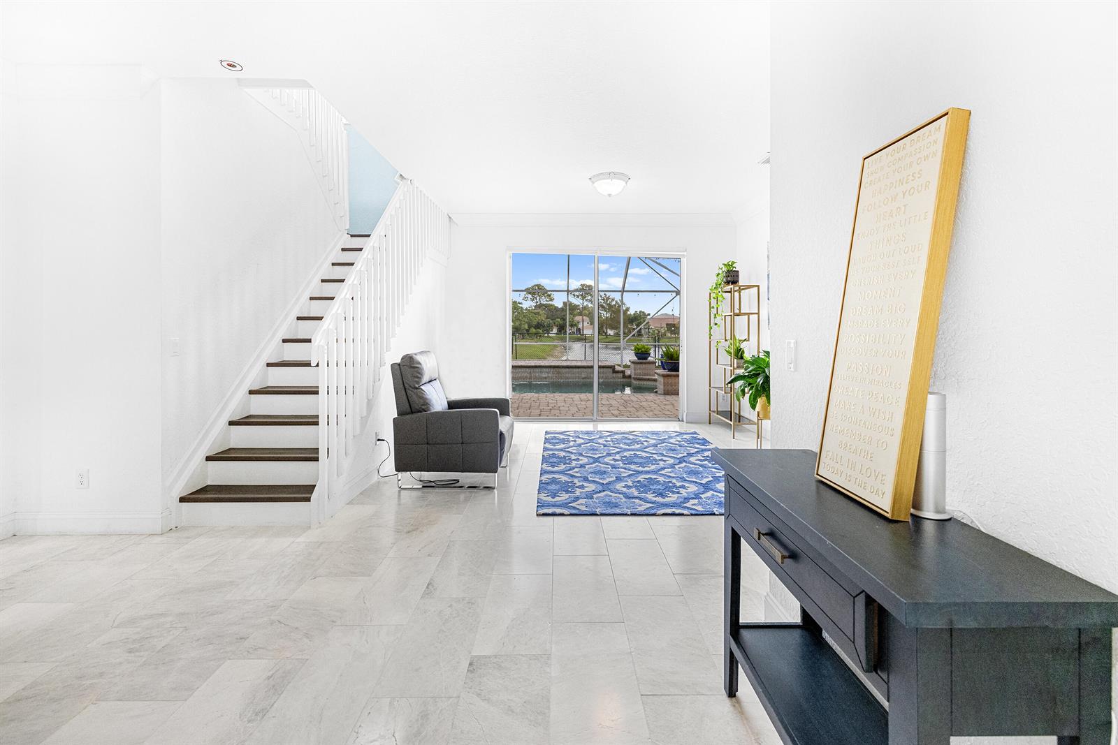 A bright living area features a staircase, tile flooring, a blue rug, and pool views — 6575 Spring Meadow Drive, FL 33413, FL