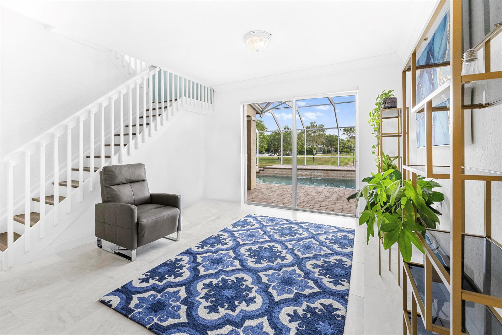A room with a staircase, a grey armchair, a blue patterned rug, and a pool view — 6575 Spring Meadow Drive, FL 33413, FL