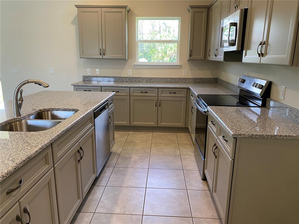 A kitchen features gray cabinets, granite countertops, stainless steel appliances, and light-colored tile flooring — 2139 GASCOM STREET, NORTH PORT, FL
