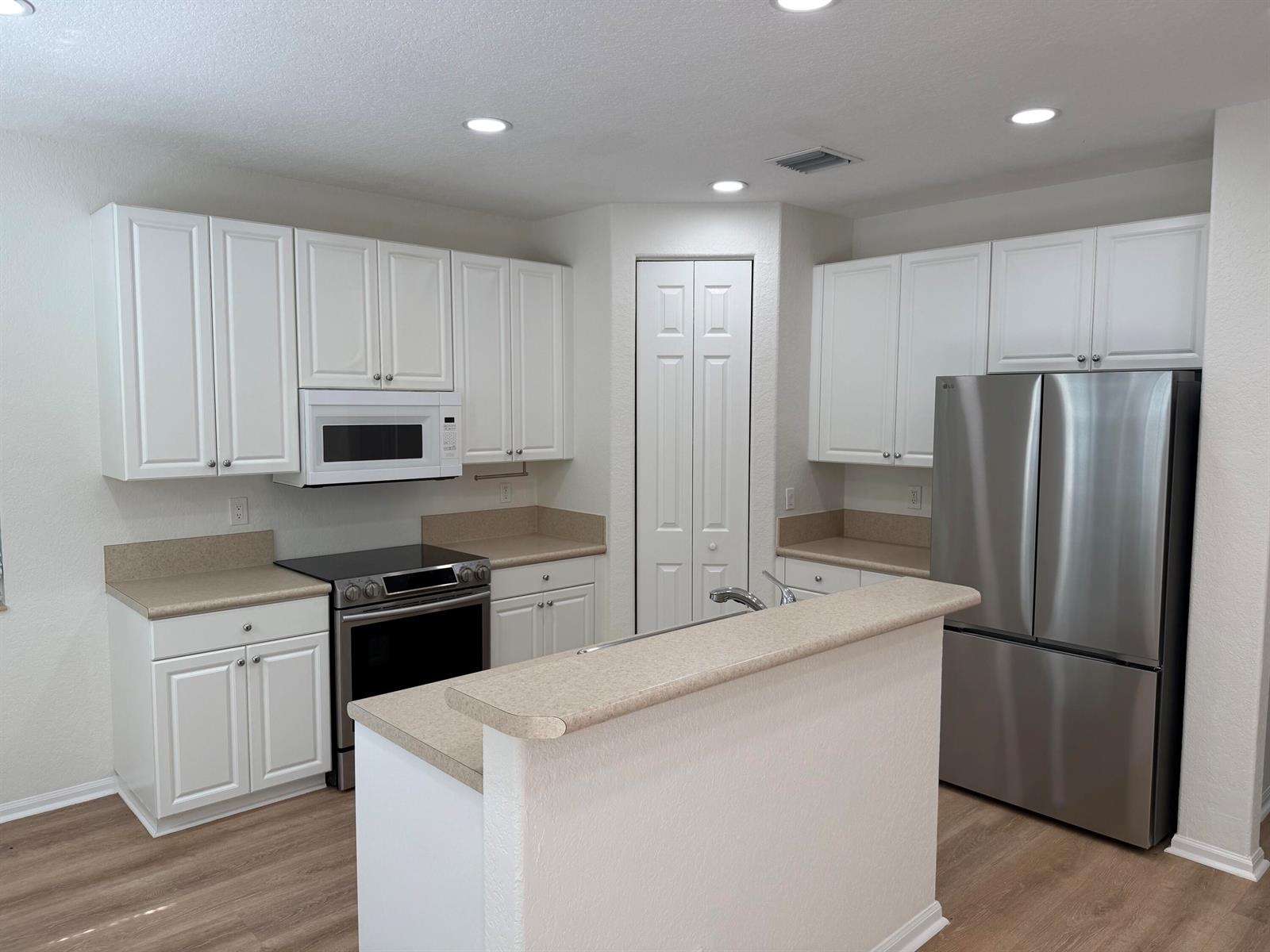 A kitchen features white cabinets, stainless steel appliances, and tan countertops with a breakfast bar — 4456 Regal Court, Delray Beach FL 33445, DELRAY BEACH, FL