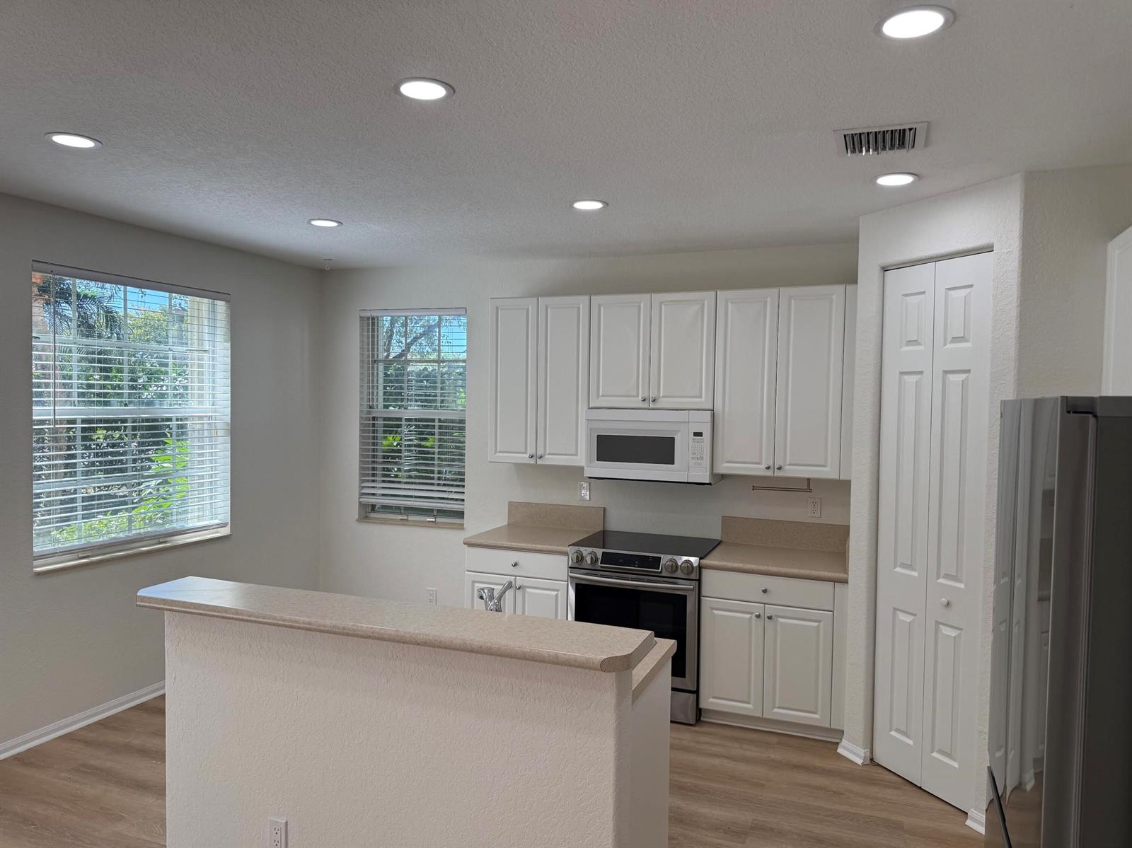 A kitchen features white cabinets, tan countertops, stainless steel appliances, and light wood-look flooring — 4456 Regal Court, Delray Beach FL 33445, DELRAY BEACH, FL