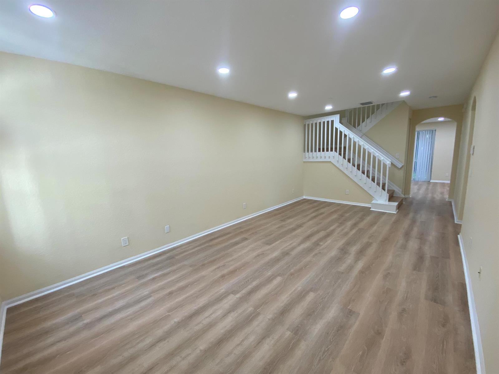 An empty living room features light-colored walls, wood-look flooring, recessed lighting, and a staircase — 4456 Regal Court, Delray Beach FL 33445, DELRAY BEACH, FL