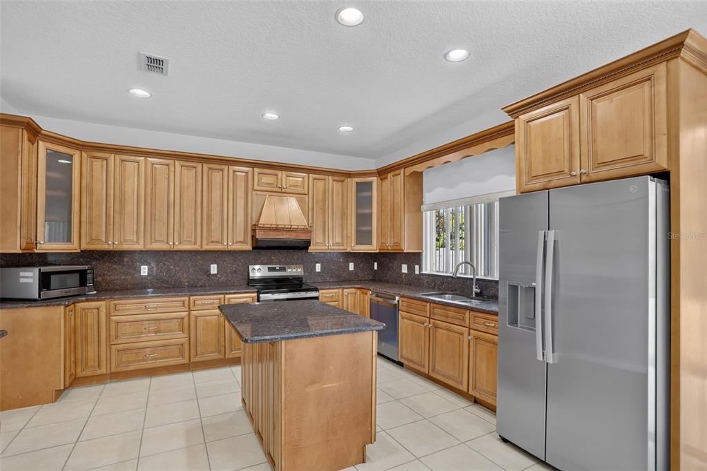 A kitchen features light wood cabinets, dark granite countertops, a center island, and stainless appliances — 2521 BARWICK STREET, ORLANDO, FL