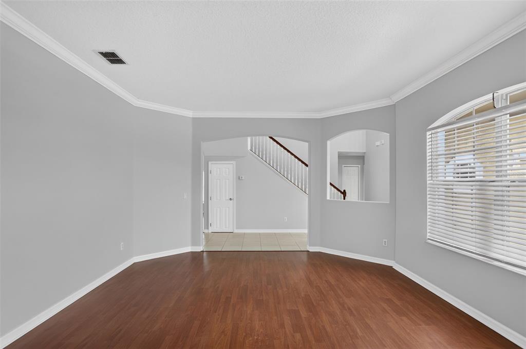 An empty room with wood-look flooring, gray walls, crown molding, and an arched entryway — 2521 BARWICK STREET, ORLANDO, FL
